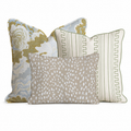 The Abstract Annie Trio Throw Pillow Bundle by Hillcroft Home features three decorative pillows: one with a green and gold floral motif, another with a geometric green and white pattern, and a smaller beige pillow adorned with delicate white speckles, all arranged against a white background.