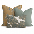 The Birdie Mae Trio Throw Pillow Bundle by Hillcroft Home features three decorative pillows—a mustard yellow pillow with a blue floral pattern, a solid sage green pillow, and a rectangular pillow in front with a bold green and white leaf design—all artfully arranged together on a white background.