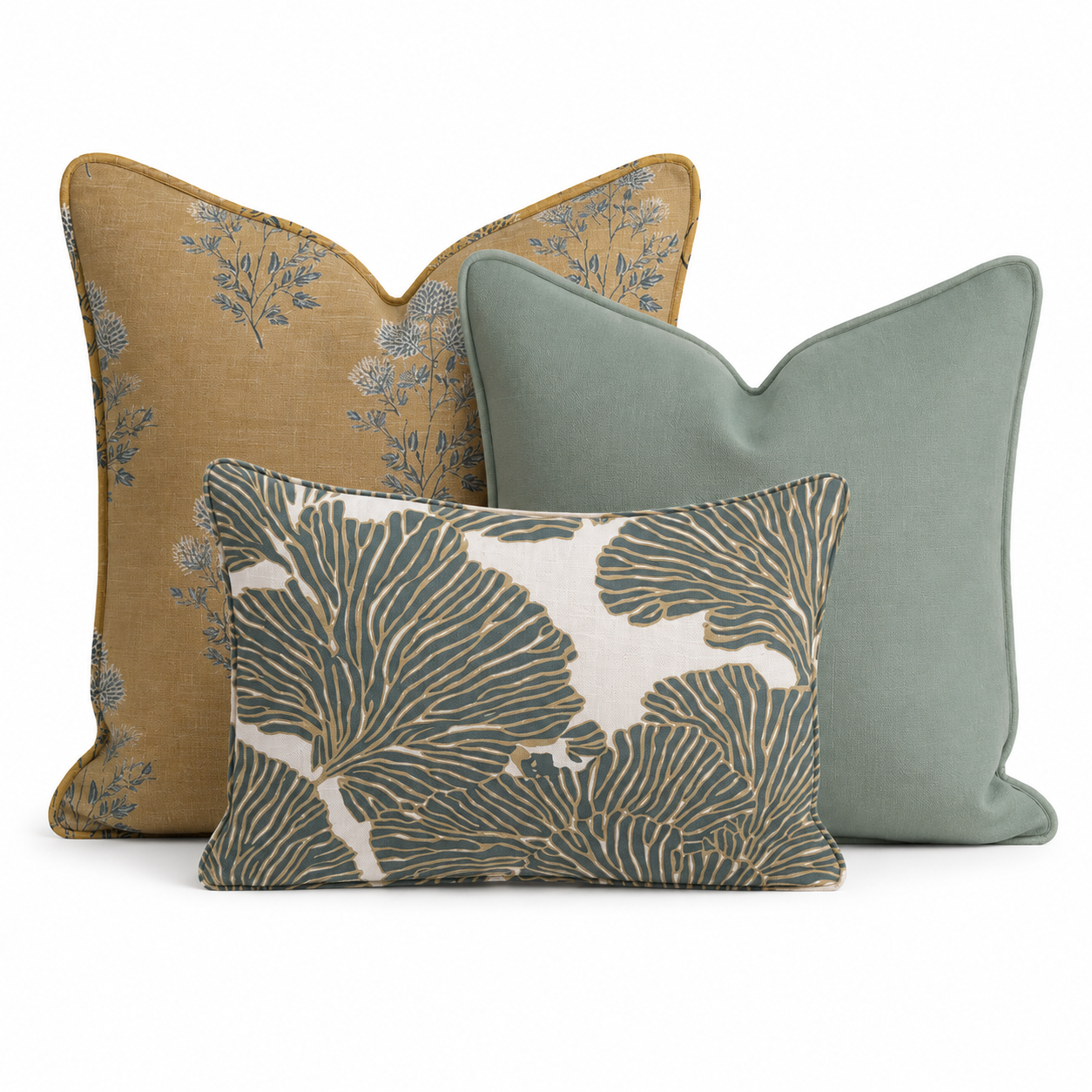 The Birdie Mae Trio Throw Pillow Bundle by Hillcroft Home features three decorative pillows—a mustard yellow pillow with a blue floral pattern, a solid sage green pillow, and a rectangular pillow in front with a bold green and white leaf design—all artfully arranged together on a white background.