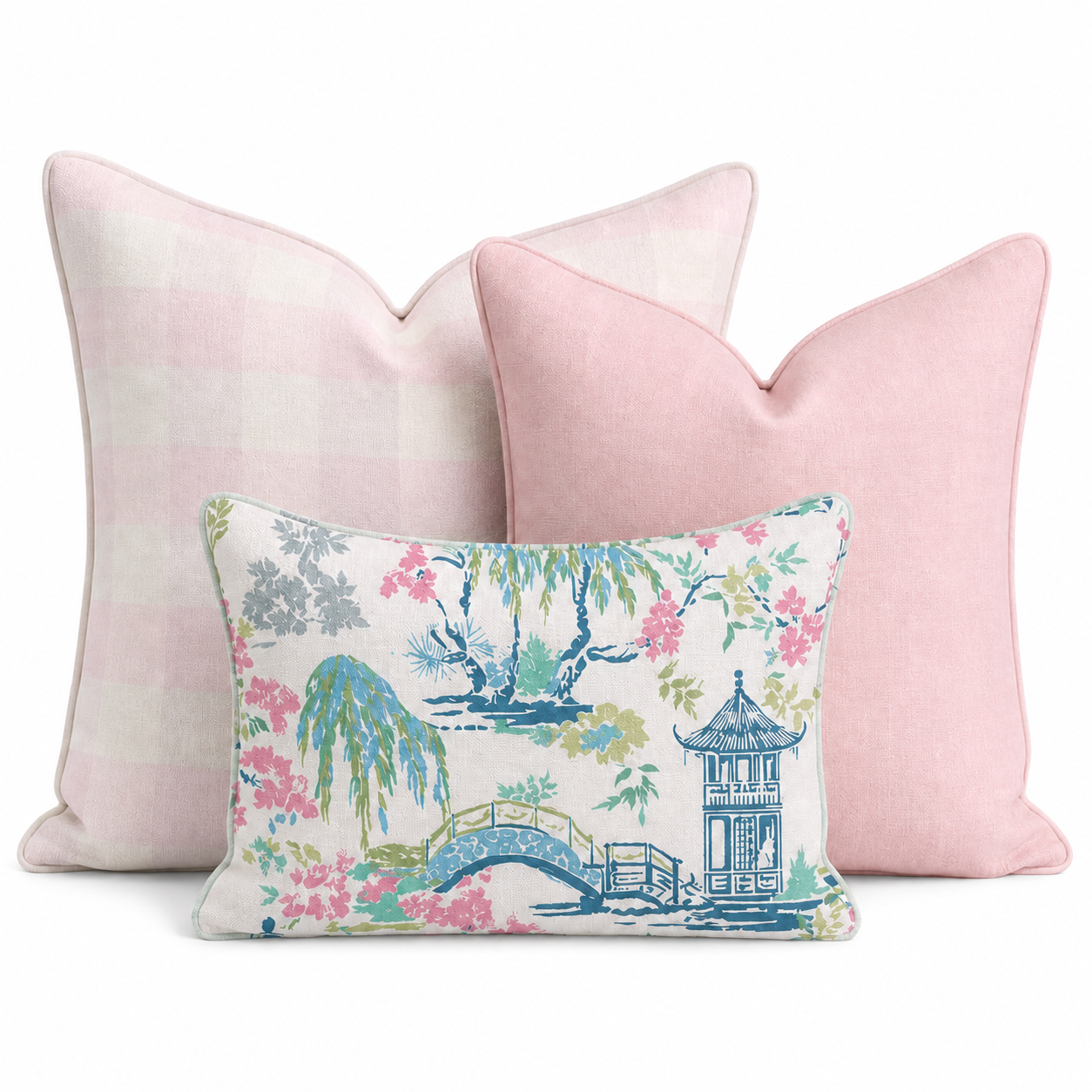 The Lotus & Willow Trio Throw Pillow Bundle by Hillcroft Home features three decorative pillows: two large pillows—one with a pink check pattern and one in solid pink—and a smaller front pillow adorned with a floral and pagoda print in pink, green, blue, and white. All are arranged against a white background.