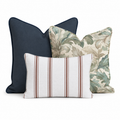 The Cordelia Trio Throw Pillow Bundle by Hillcroft Home features three decorative pillows—one solid navy, one with a green leaf pattern, and one rectangular white pillow with brown stripes—arranged together on a white background.